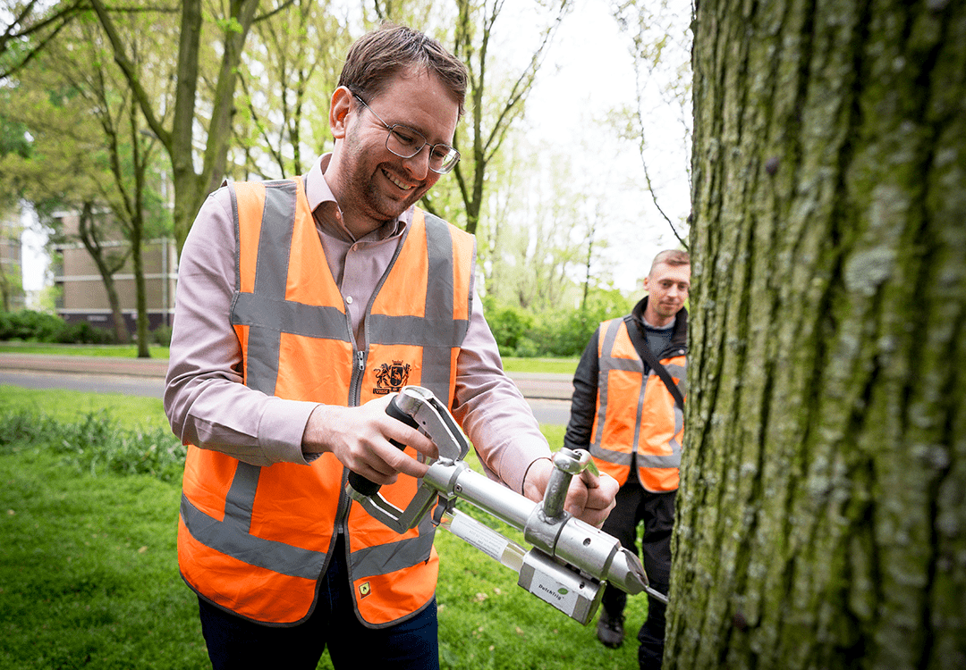 Aan de Volendamlaan zet wethouder Robert Barker van Buitenruimte, Dierenwelzijn en Milieu de eerste Haagse prik van dit jaar onder toeziend oog van boomverzorger Rick. De foto is gemaakt door Valerie Kuypers voor het Haagse Groen